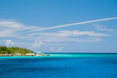 A moored boat off the green shoreline of Catalina Island amid bands of turquoise Caribbean water, Dominican Republic