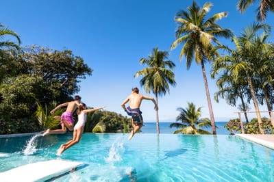 A traveler leaping into an infinity pool framed by palms above the ocean