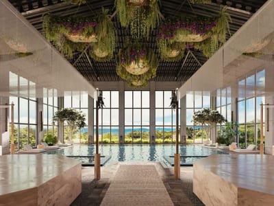 Indoor spa pool at Hacienda AltaGracia under a vaulted dark-wood ceiling hung with cascading greenery and purple flowers, floor-to-ceiling windows framing the Pérez Zeledón mountains, Costa Rica